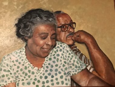 A painting depicts the author's mother and father at an older age. The woman is wearing a white shirt with green splotches, and her curly dark hair, which is graying at the temples, is pulled back into a bun. She's looking down and smiling, her dimples on display. Just behind her sits her husband, who is resting his right fist contemplatively against his chin and looking at the camera. He's wearing glasses and a striped, short-sleeved shirt, and has a graying mustache. The background is a light brown.